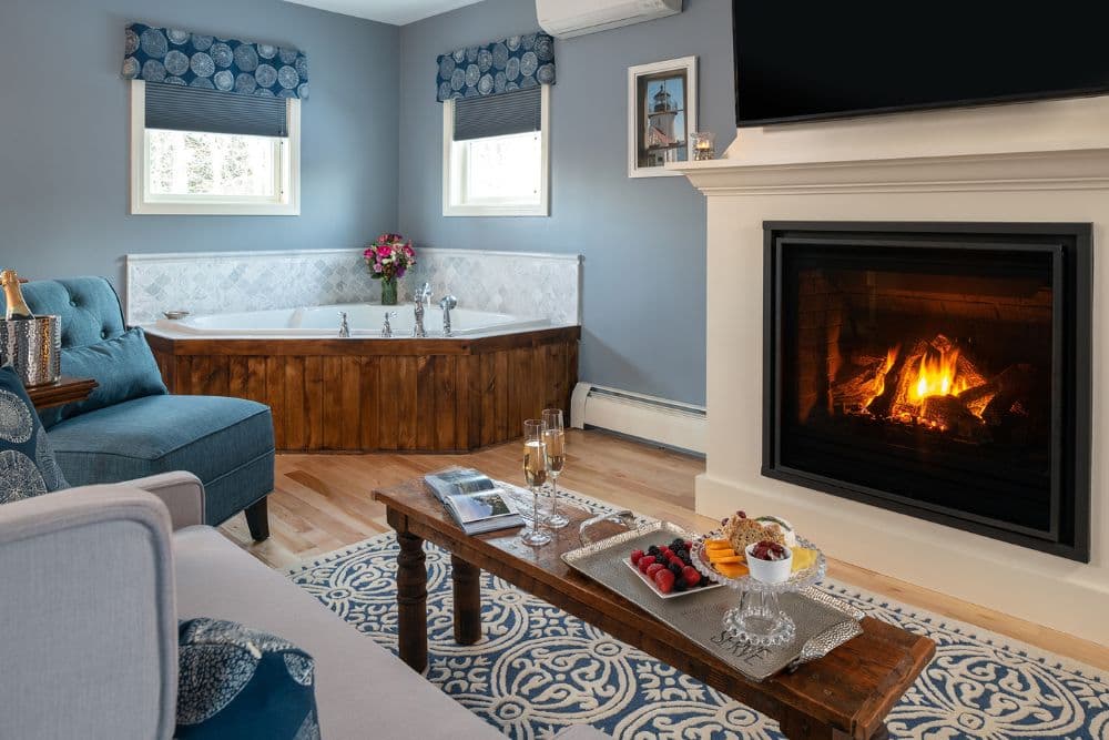Cozy room featuring a fireplace, a corner jacuzzi bath, and a small table with fruits and drinks.